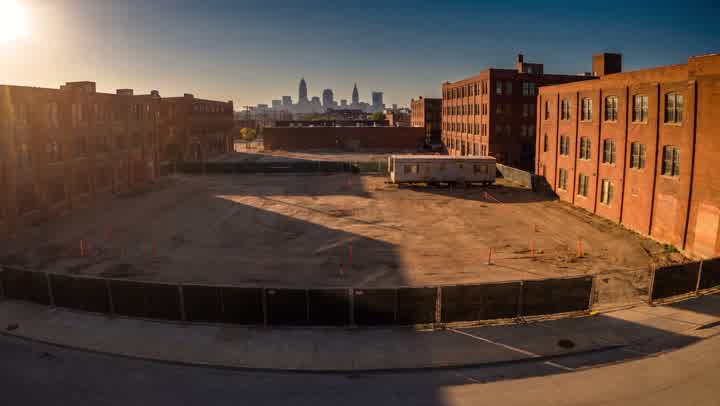 An empty construction lot between brick warehouses at golden hour, which becomes a finished four-storey building as you scroll